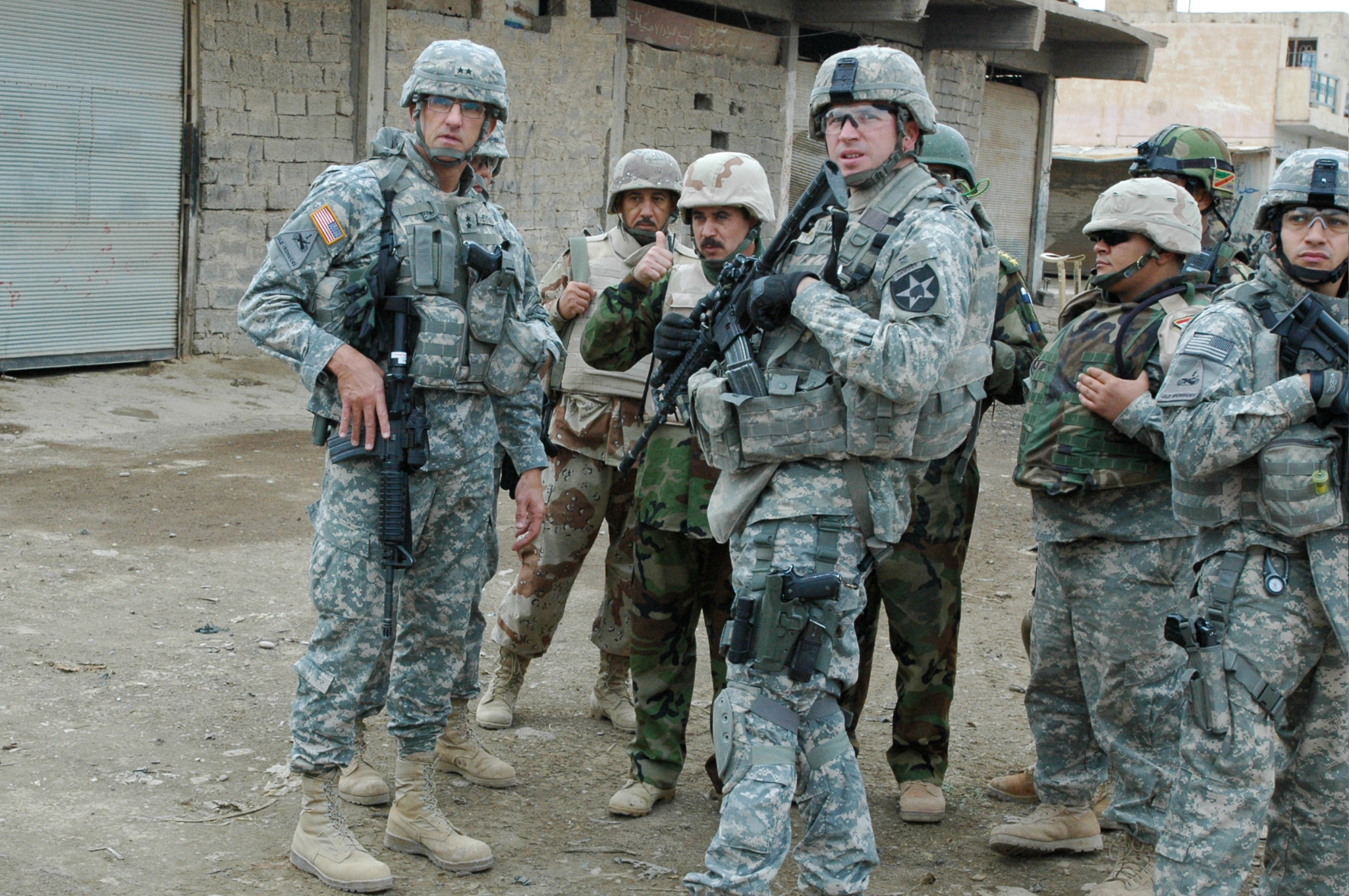 Group of soldiers in military gear standing on a dusty street in a war-torn area.
