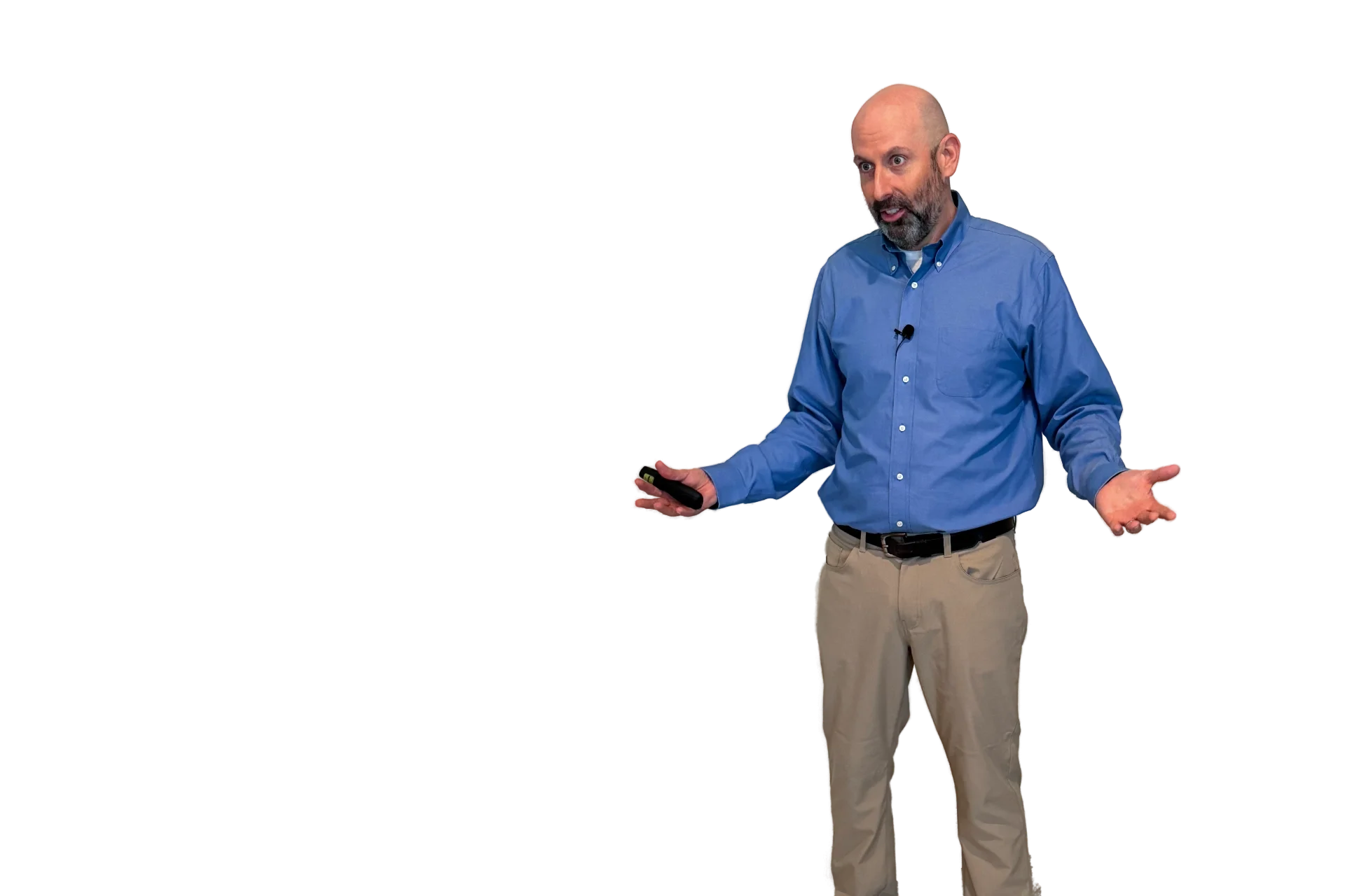 John with a beard, wearing a blue button-up shirt and khaki pants, stands with one hand slightly raised and the other holding a remote, as if giving a presentation or speaking.