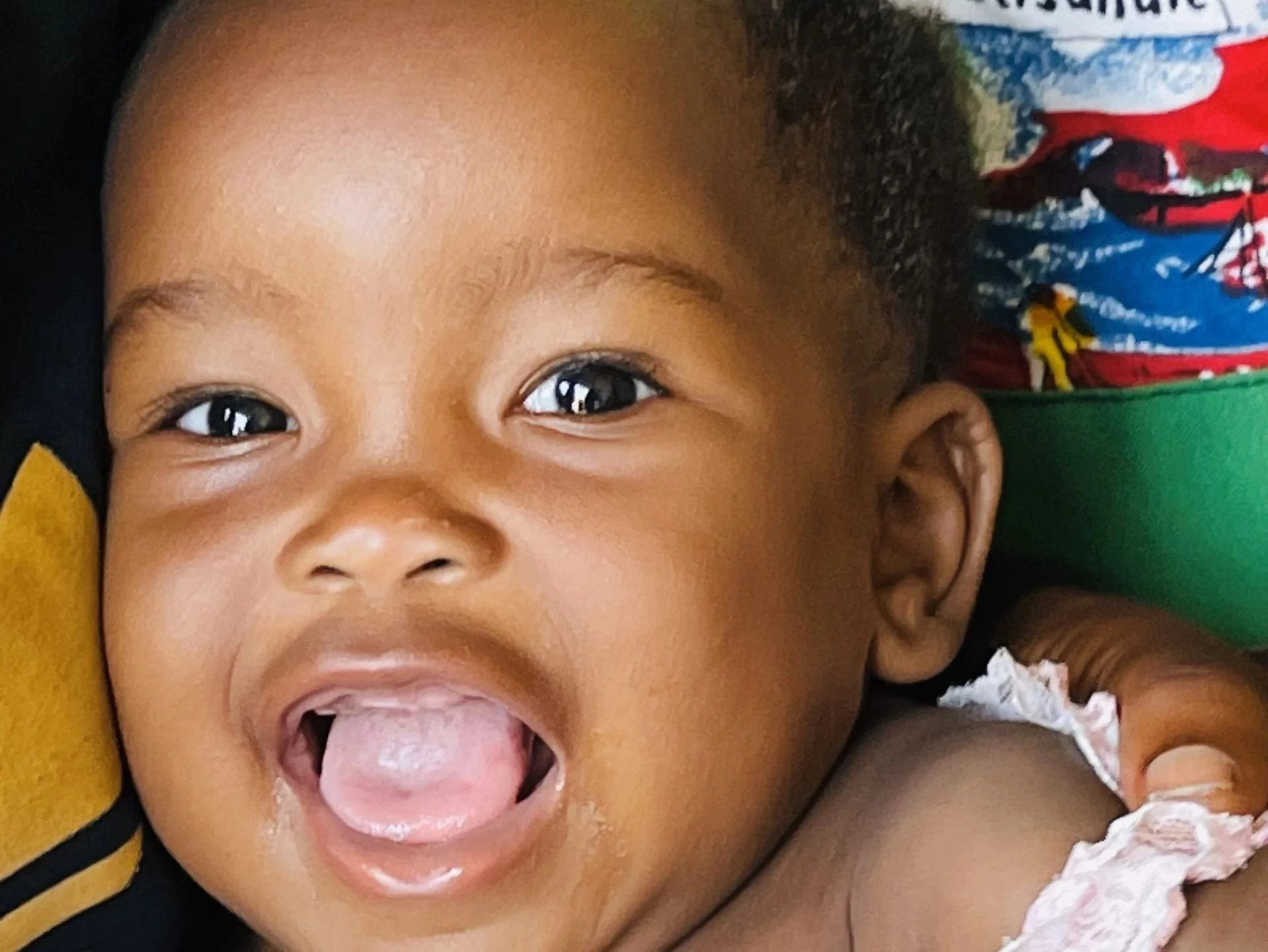Close-up of a smiling young child with dark hair and big eyes, sticking out their tongue.