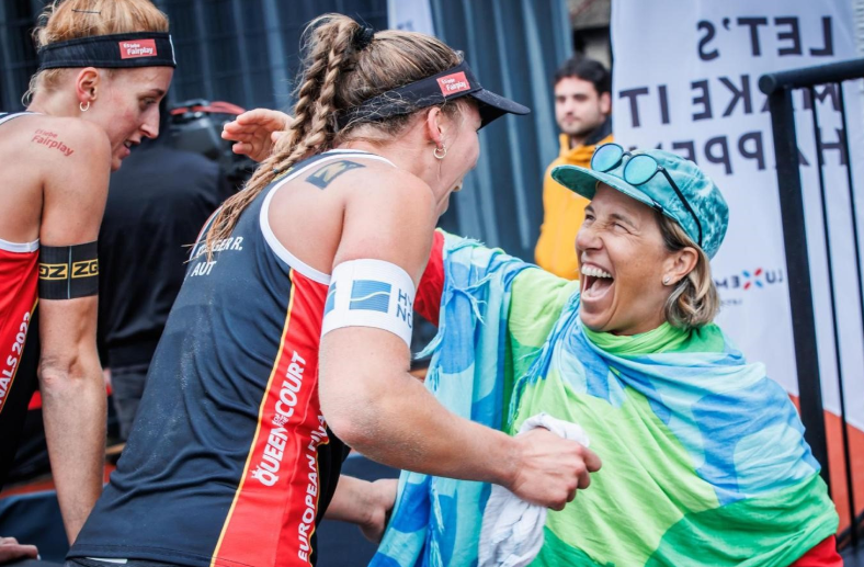 Weiblicher Coach mit Beachvolleyball Team - Vorbild für das Projekt und zeigt auf für Gemeinschaft, Sichtbarkeit und Frauenförderung im Sport