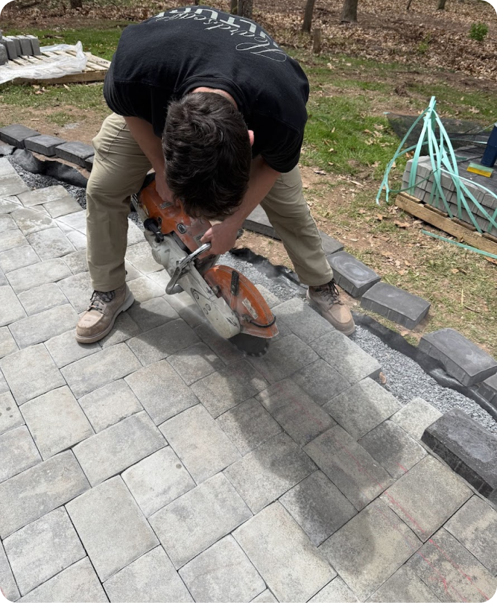 A man is cutting and laying gray stone pavers for a walkway outdoors.