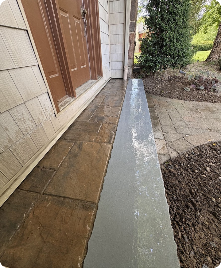 Close-up of a house entryway showing a brown door, stone and brick pathway, and a newly poured concrete step.