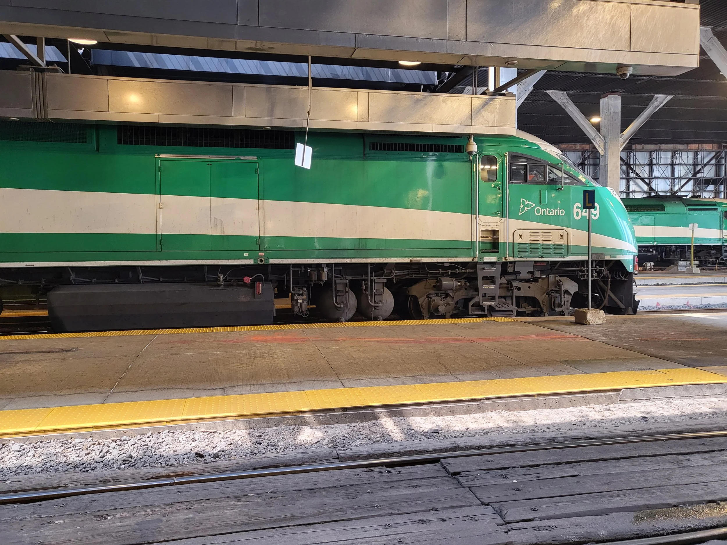 Green and white Ontario train on a platform at a train station with rail tracks in the foreground.
