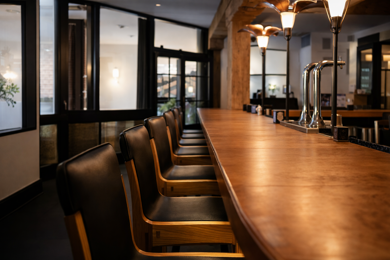 Empty bar counter with black leather and wood chairs, warm lighting, and black napkin holders