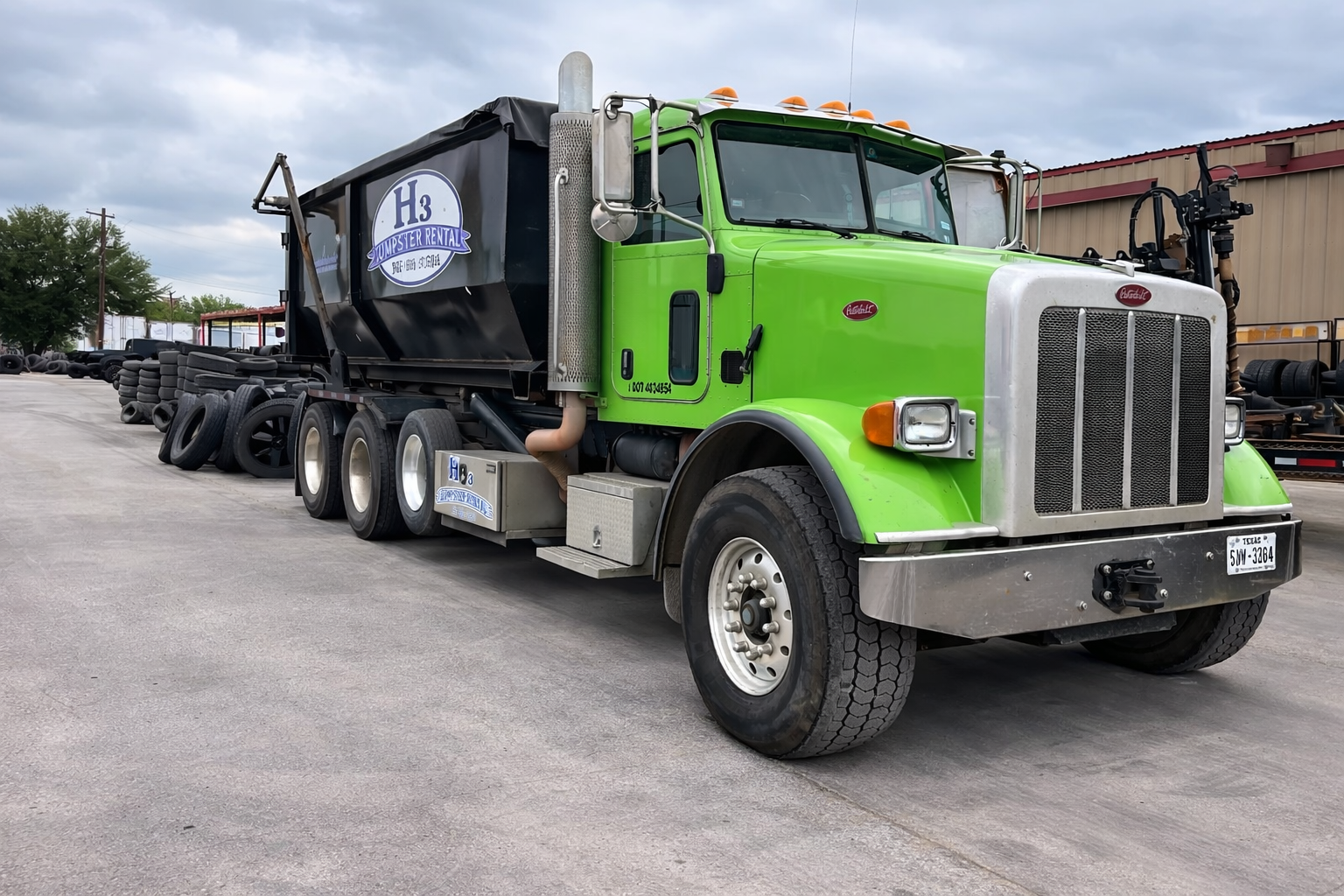 A green and white flatbed truck loaded with tires parked in an outdoor lot.
