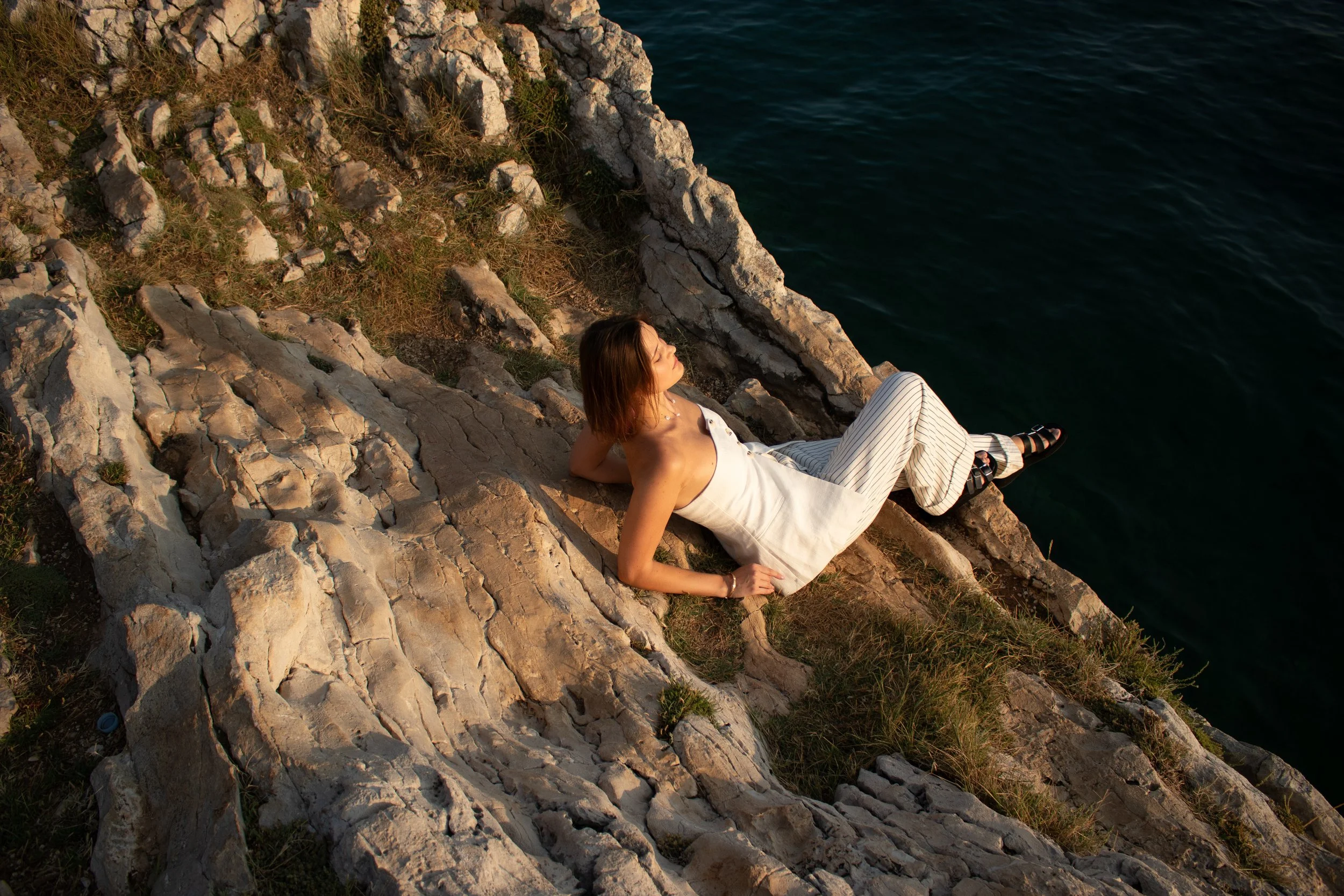 Female solo traveler enjoys the seaview in Croatia during sunset. Warm light, flowing dress and peaceful seaside scenery create a natural, aesthetic and cinematic travel moment.