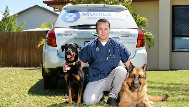 Dr Jeremiah kneeling behind his work vehicle with his 2 dogs
