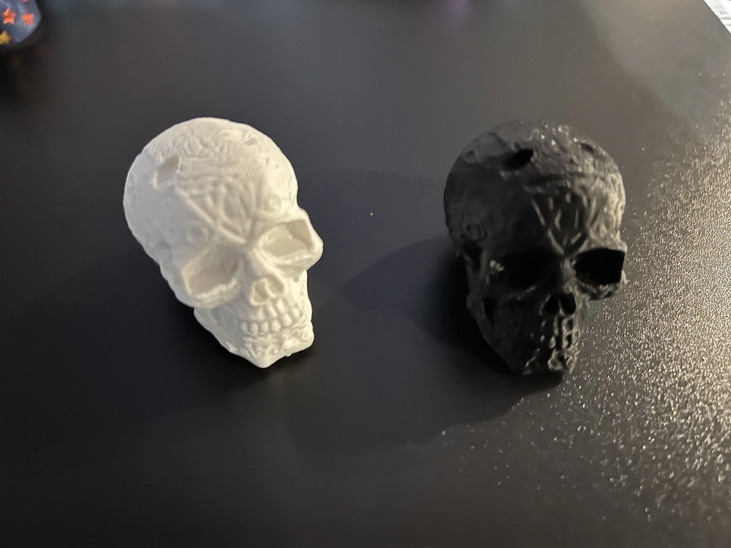 Two skull-shaped objects on a dark surface, one white and one black, both with intricate patterns.
