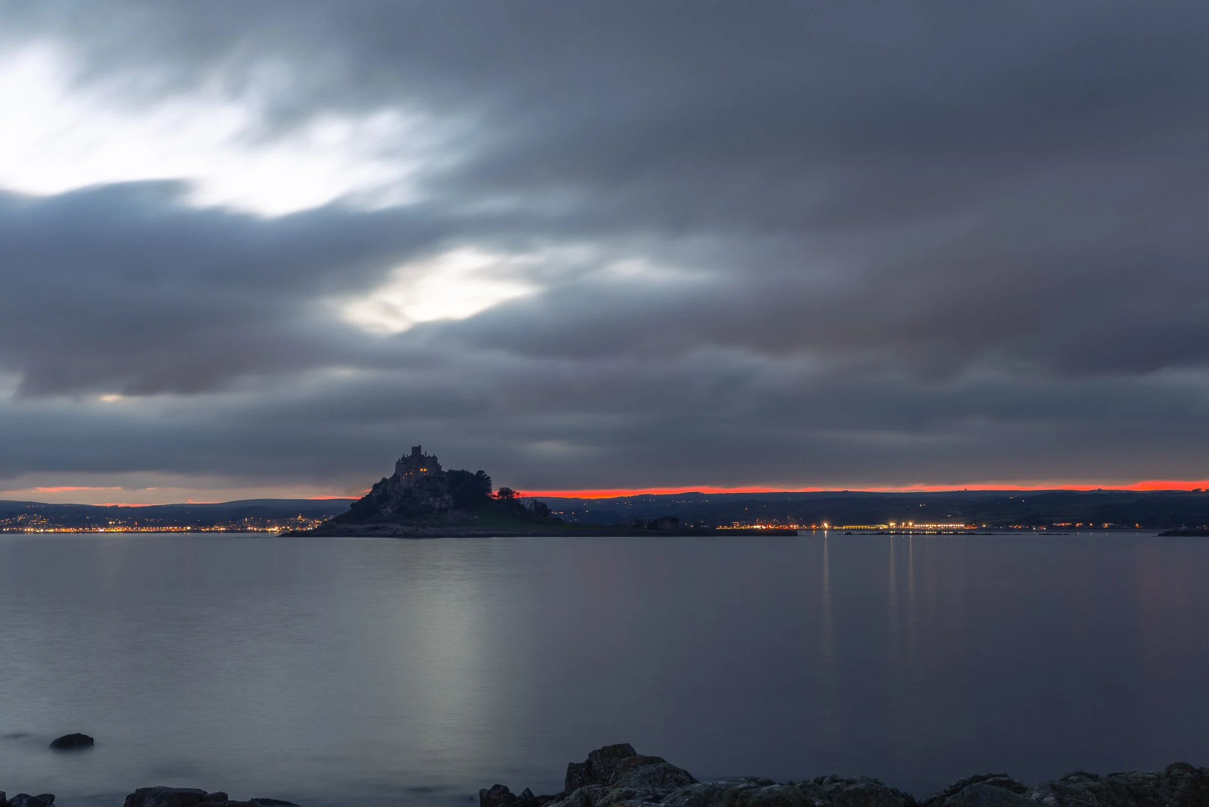 St Michael's Mount at twilight with an orange seam of fire on the horizon and Penzance lights reflecting across the bay, fine art canvas by Lowena Studios