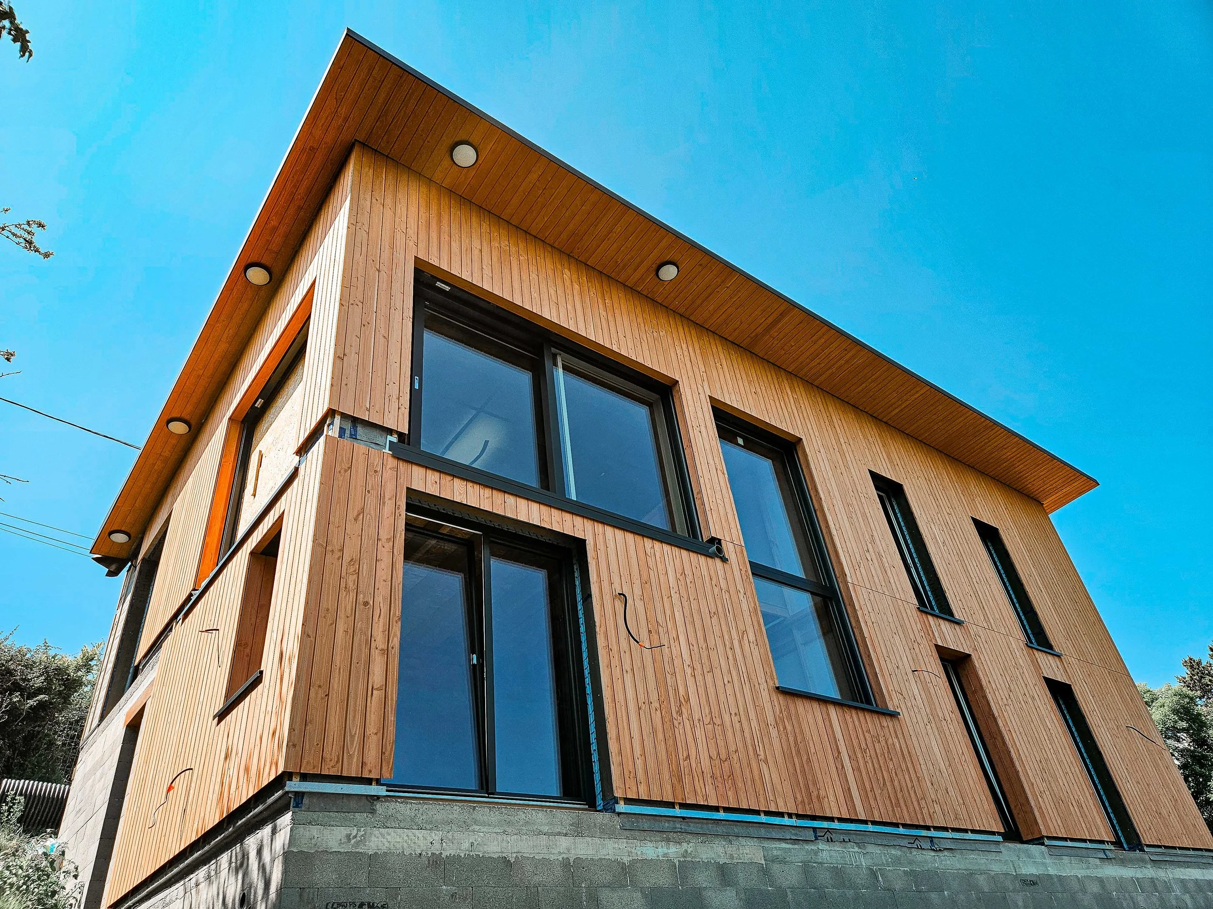 Vue d'un bâtiment en construction avec façade en bois, fenêtres en verre, sous un ciel bleu.