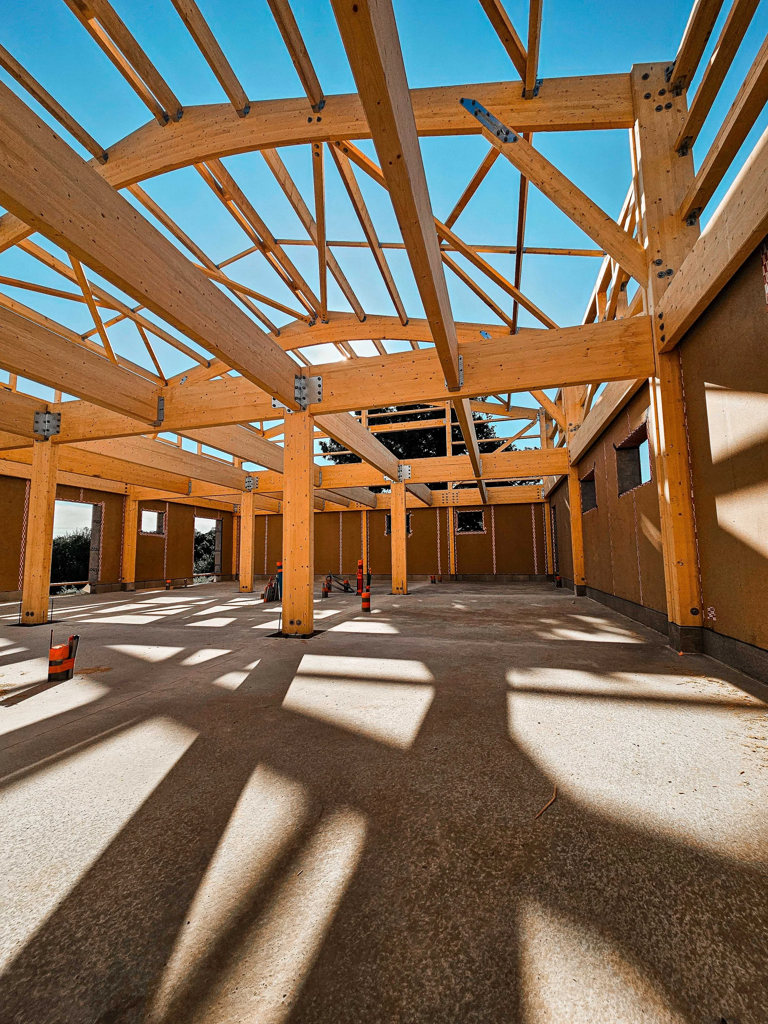 Structure en bois en cours de construction pour un bâtiment, avec rayons du soleil créant des ombres sur le sol.