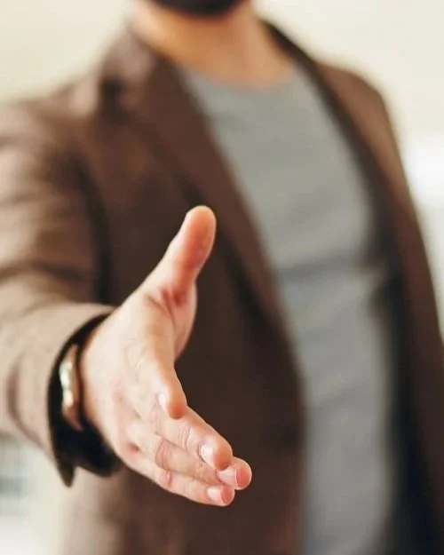 Person extending hand for a handshake, wearing a blazer.