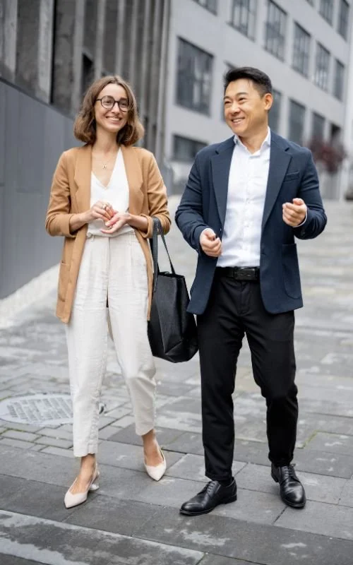 A woman and a man walking on a city sidewalk, smiling and talking.