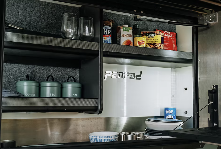 Kitchen cabinet with glassware, canned goods, boxes of food, labeled containers for coffee, tea, and sugar, plates, bowls, and a container of popcorn.