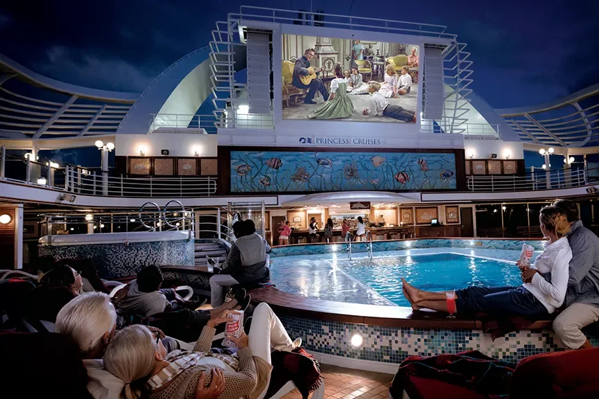 People relaxing and watching a movie on a large screen at the poolside on a cruise ship.