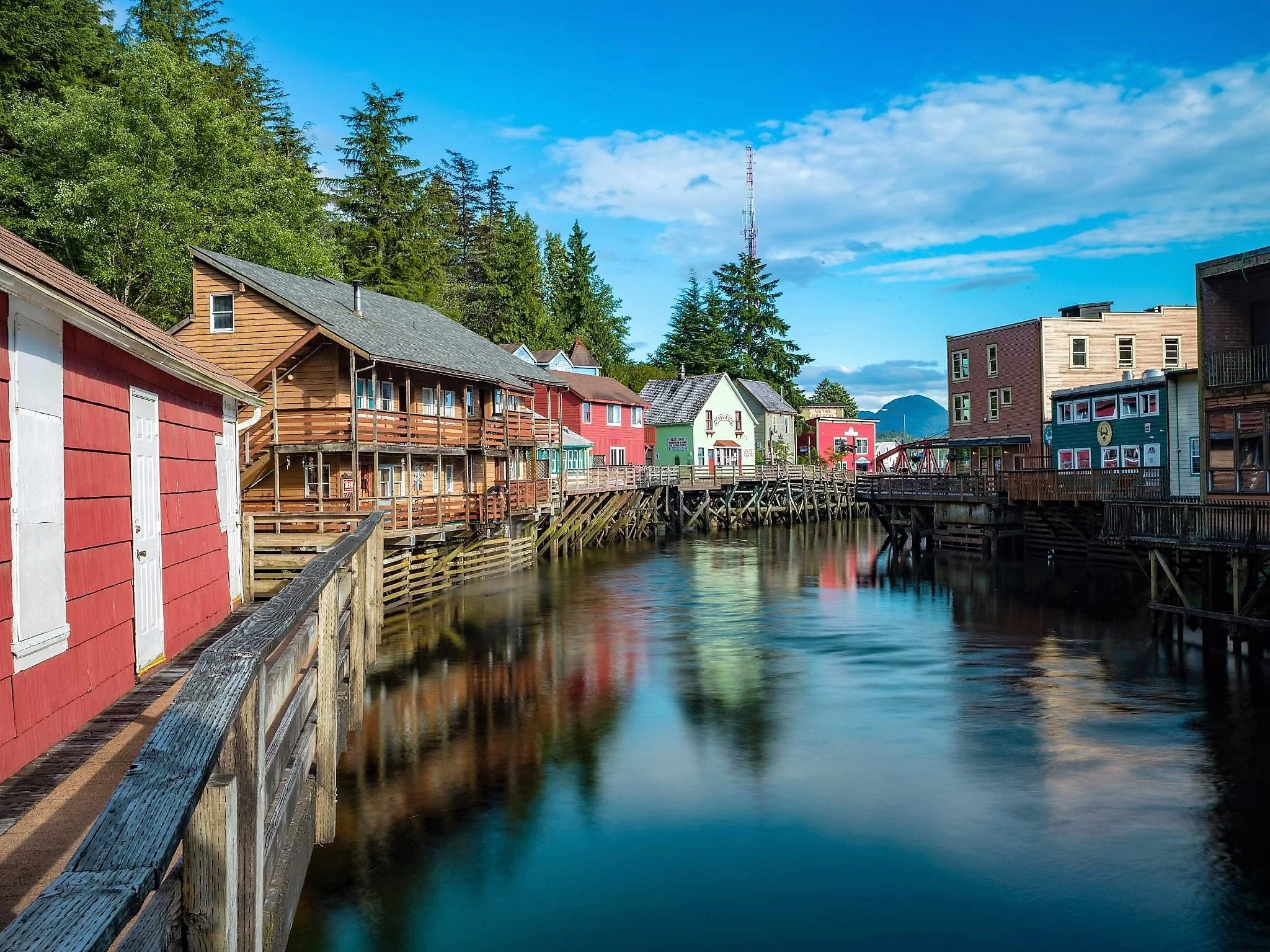 Colorful buildings along a wooden pier over water with trees and blue sky in the background.