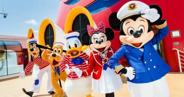 Mickey Mouse dressed as a ship captain, standing with Minnie Mouse in a red and white sailor outfit, Donald Duck and Pluto in striped sailor shirts and hats, and Goofy in a red nautical outfit. They are on a Disney cruise ship deck with a colorful ship structure in the background.