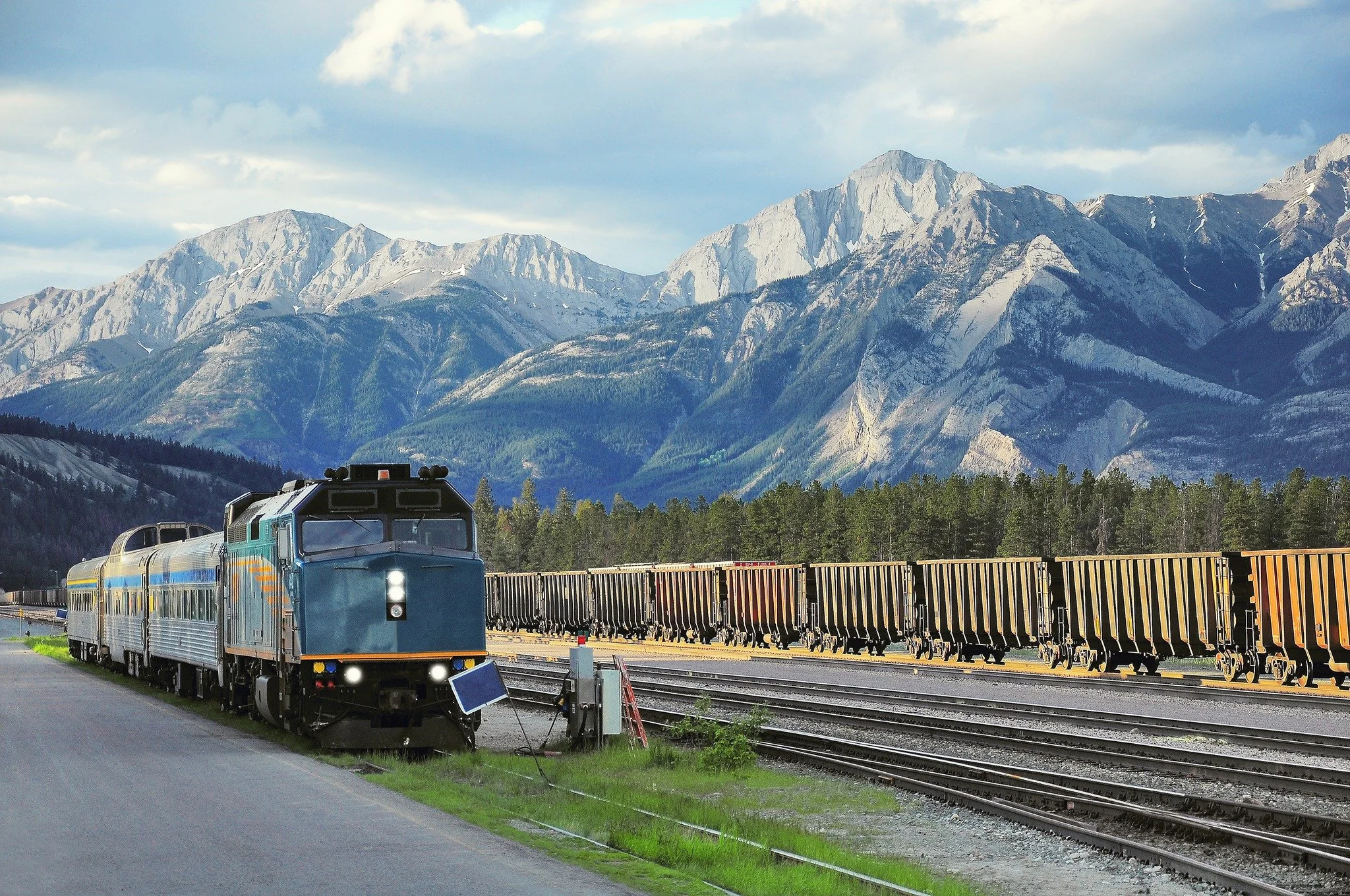 A blue locomotive train parked on tracks with mountains in the background and a row of empty freight cars on nearby tracks.