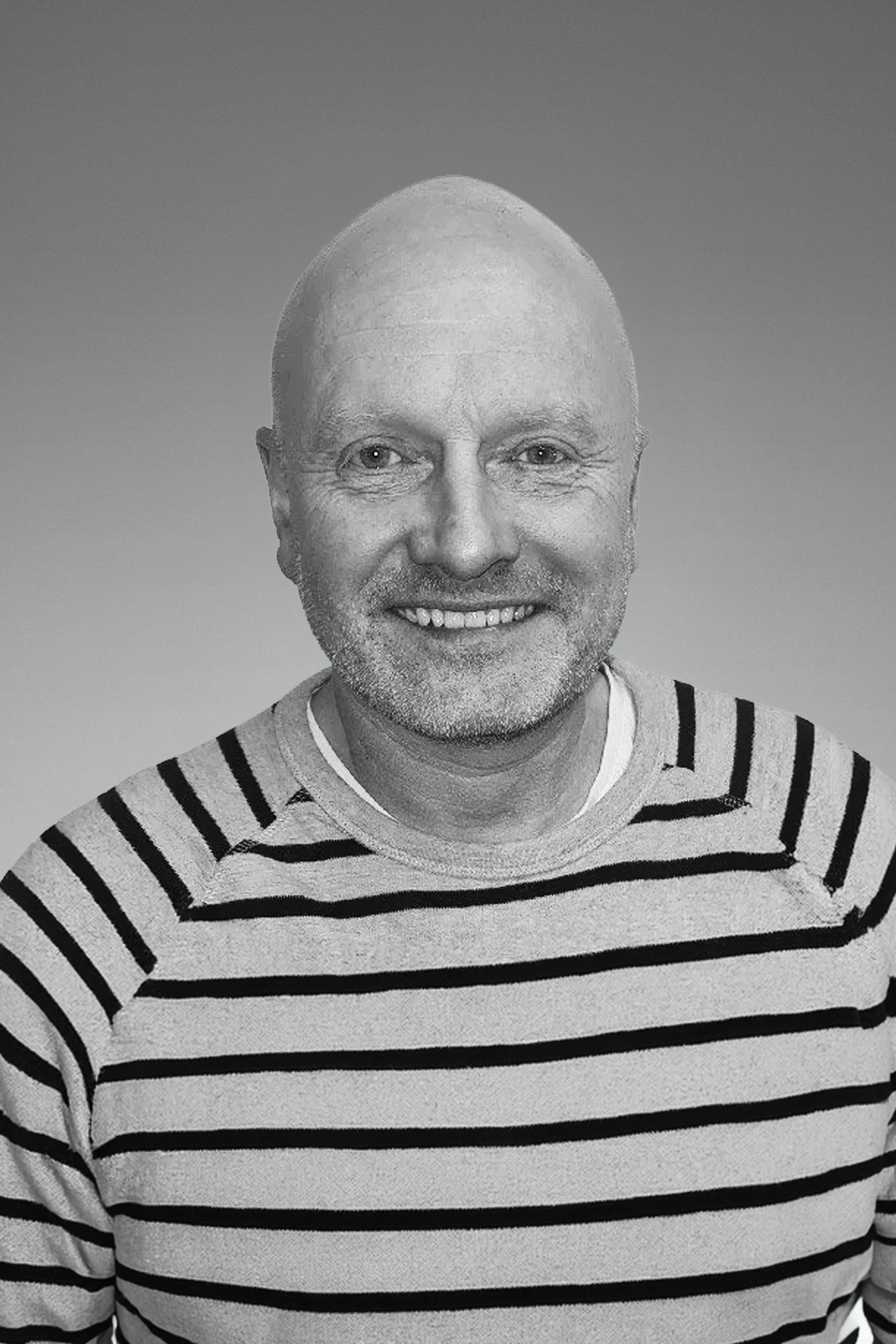 Portrait of a smiling man with a bald head, light-colored eyes, a beard, wearing a striped shirt, against a plain background.