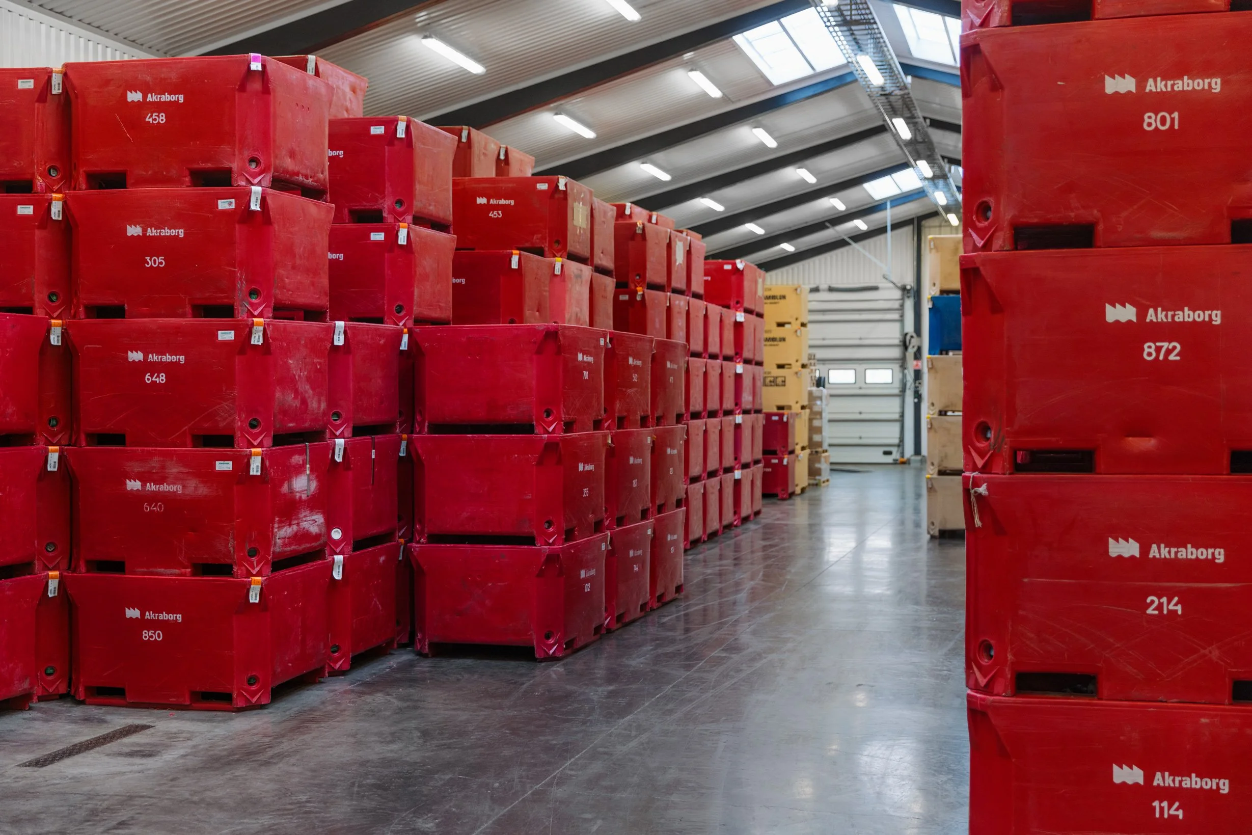 Rows of red plastic containers stacked inside a warehouse. Each container has the word 'Akroborg' and a number printed on it.