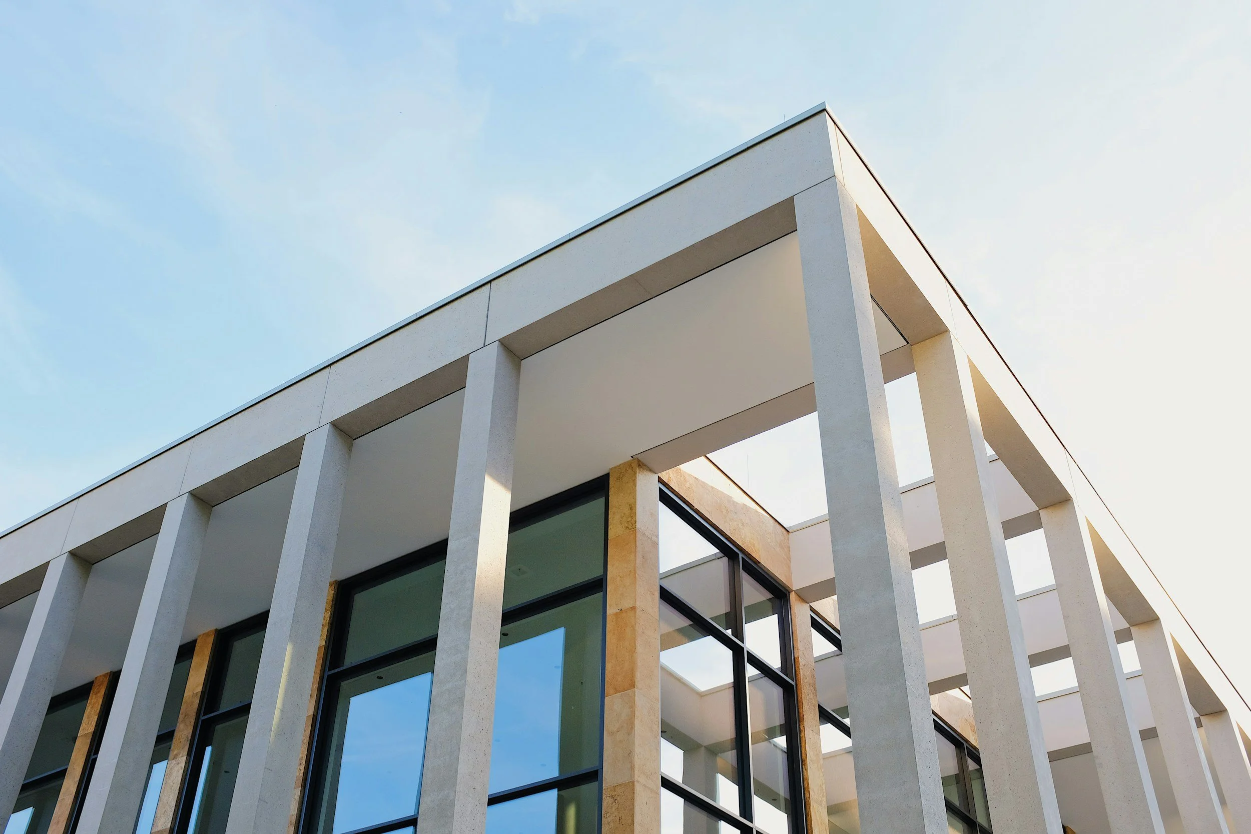 Modern building with white vertical beams, large glass windows, and beige stone accents, set against a blue sky with few clouds.