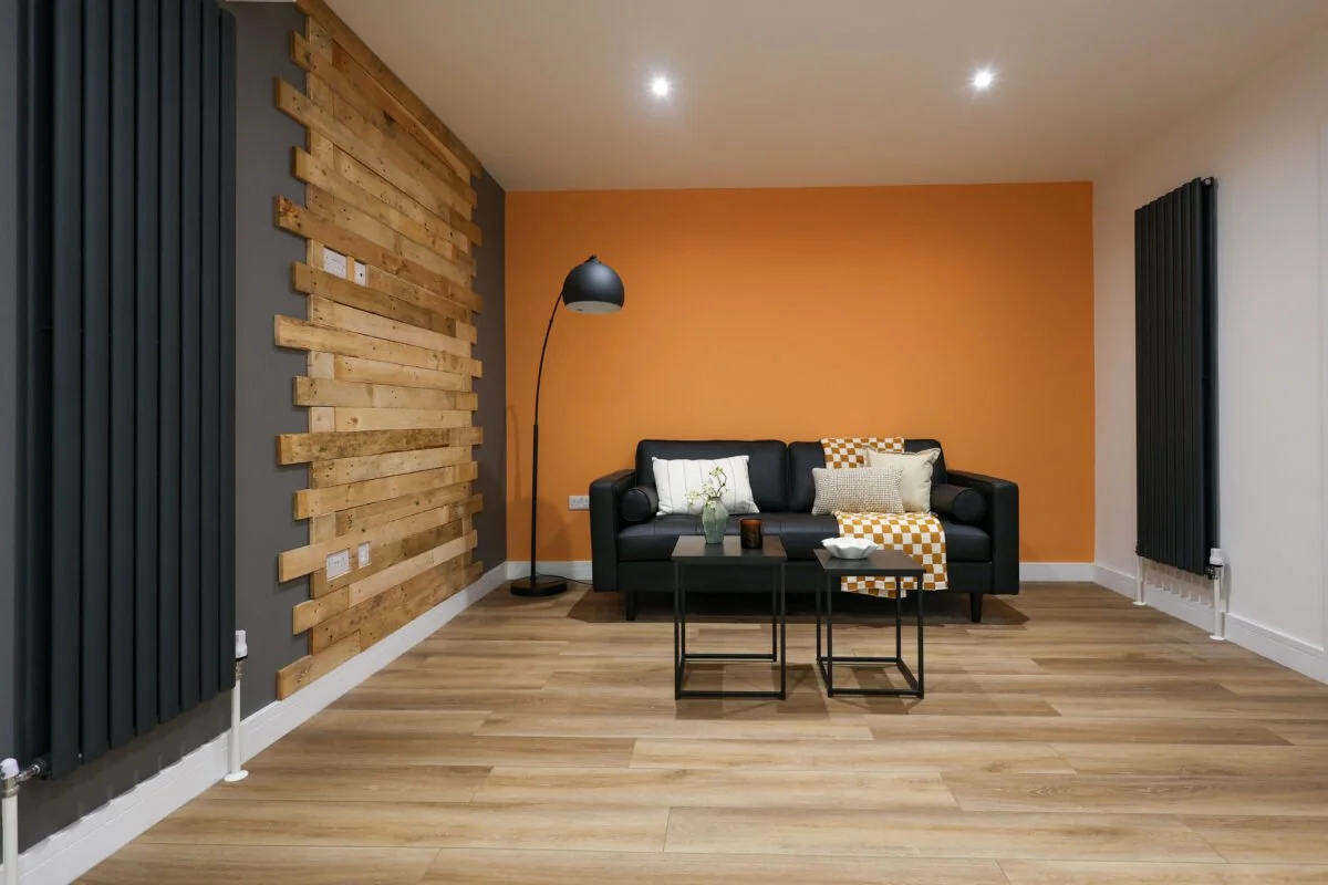 Modern living room with a black sofa, decorative pillows, a small coffee table, and a wood-paneled accent wall.
