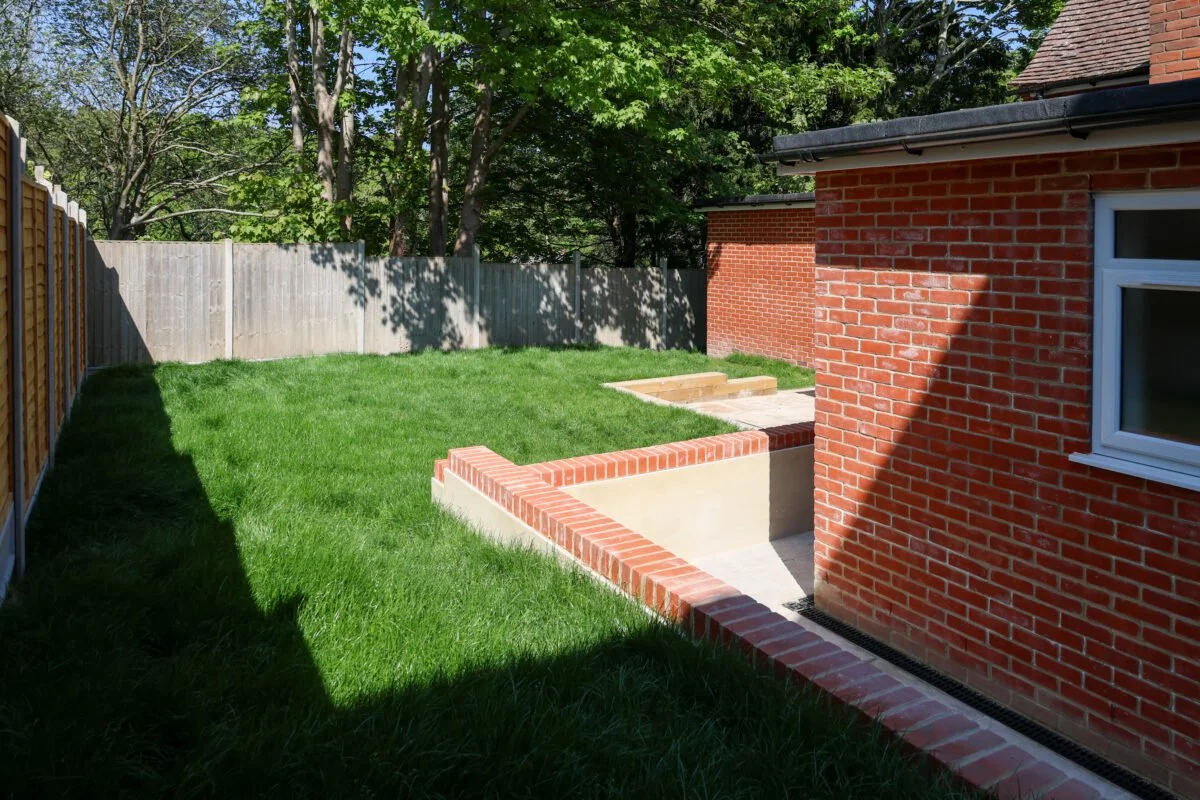 A backyard with newly laid grass, a brick house, a wooden fence, and small stairs leading to a patio.