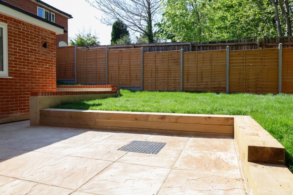 Backyard with brick house wall, tiled patio, grassy area, and wooden fence.