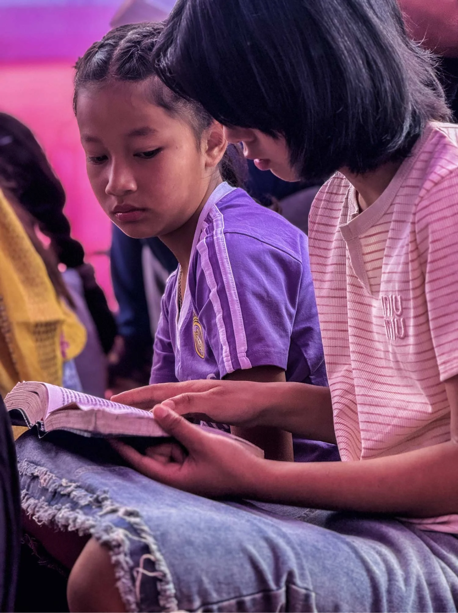 Two girls sitting closely together, looking at an open book.