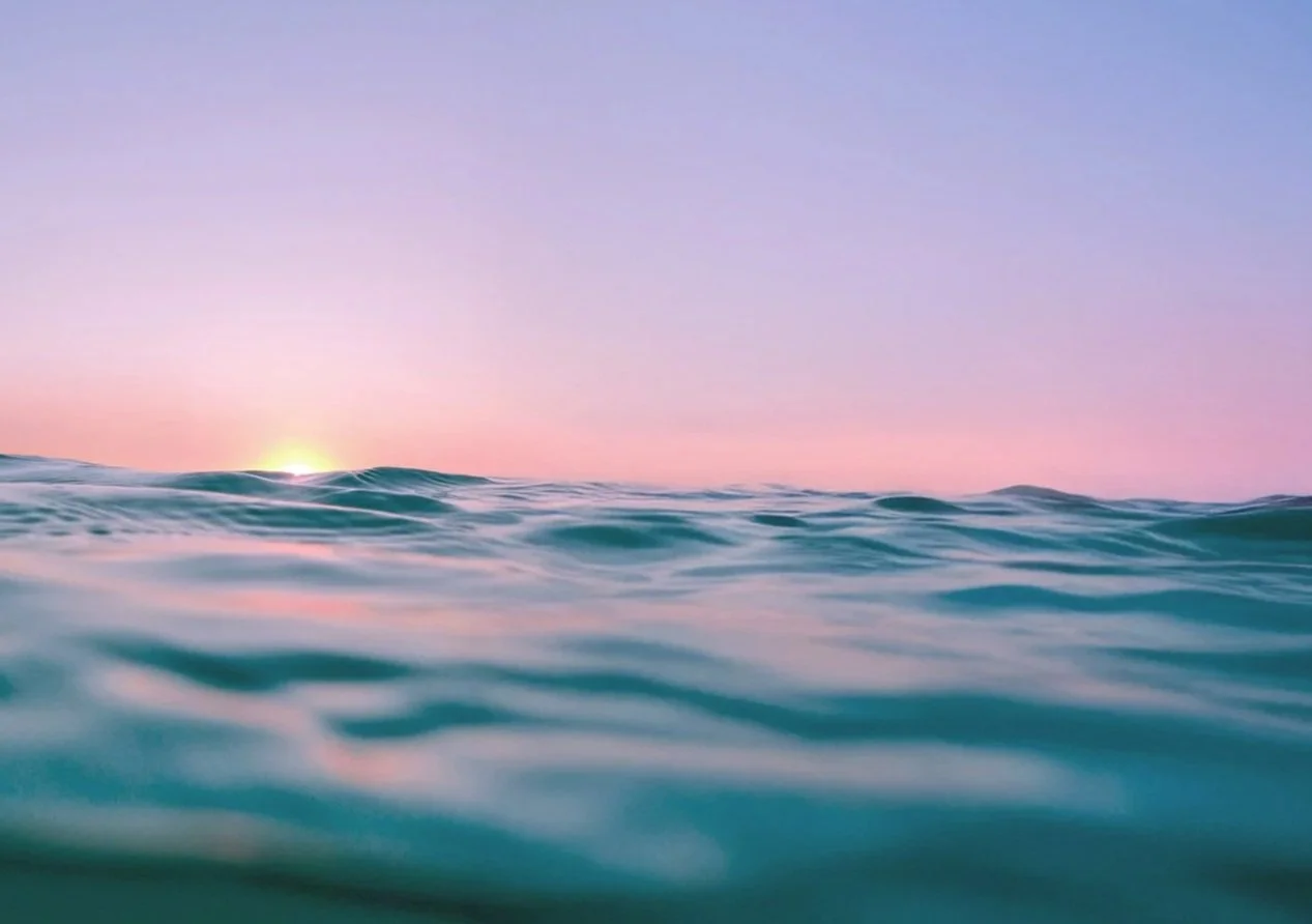 Ocean waves during sunset with a pastel pink and purple sky in the background.
