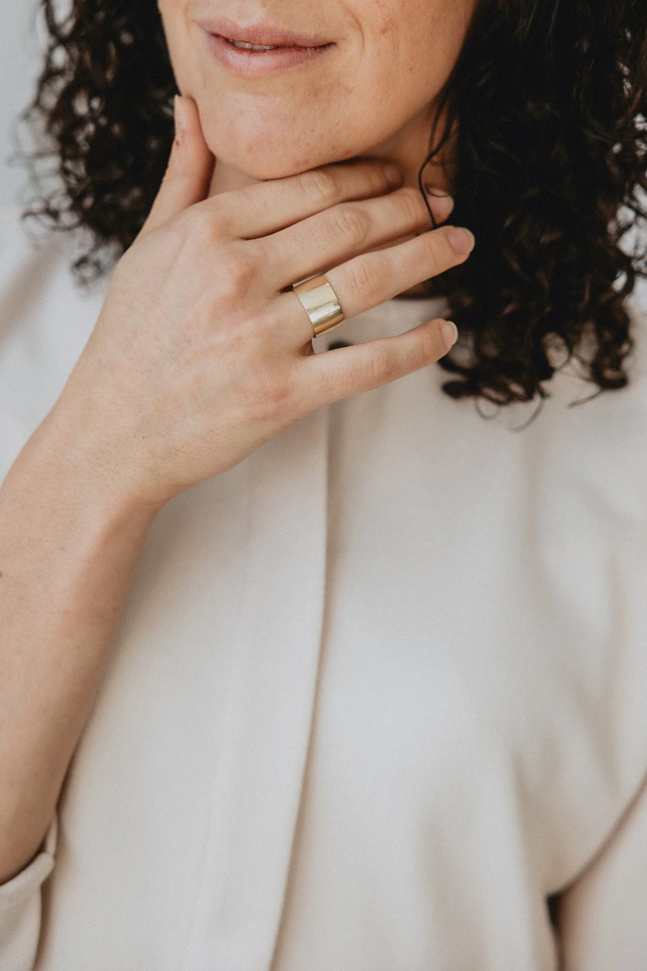 Hand met een gouden ring op de middelvinger, dicht bij de kin, met donker krullend haar op de achtergrond.
