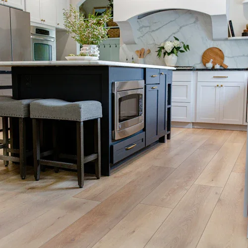 Modern kitchen with navy blue island, light gray bar stools, white cabinets, marble backsplash, and wooden flooring.