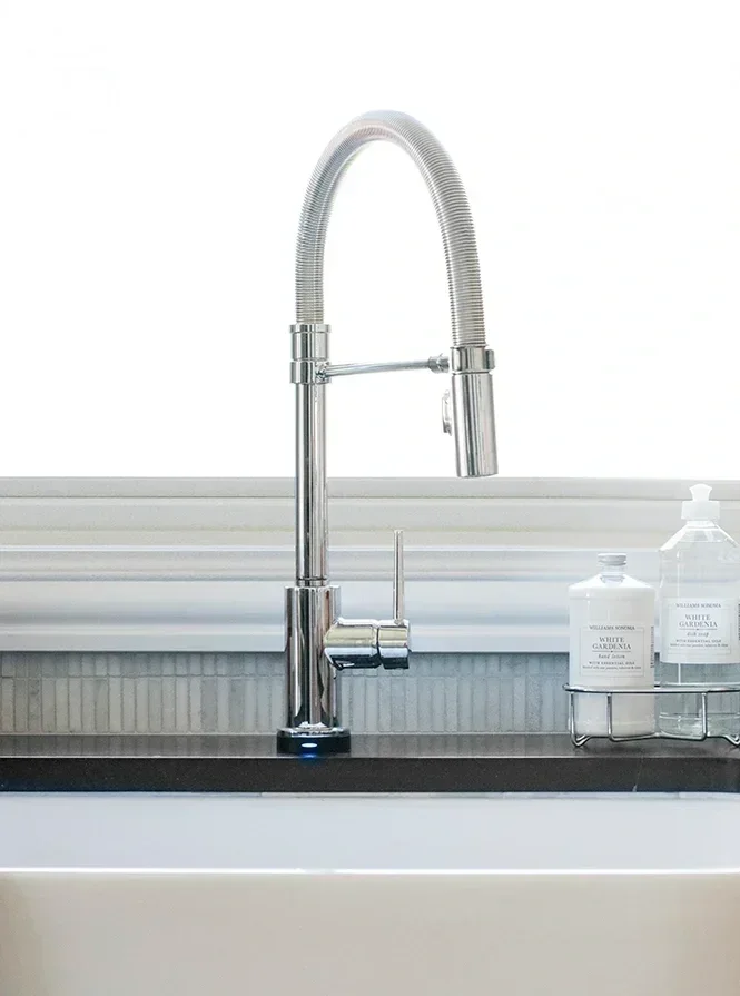 Modern kitchen sink with a tall, curved, chrome faucet and two soap dispensers on a metal rack.