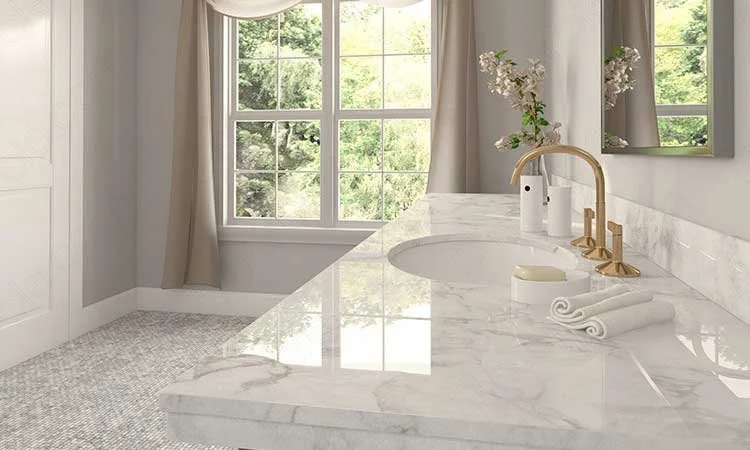 Bathroom with a marble countertop, gold fixtures, a sink, a vase with white flowers, and a large window with green trees outside.