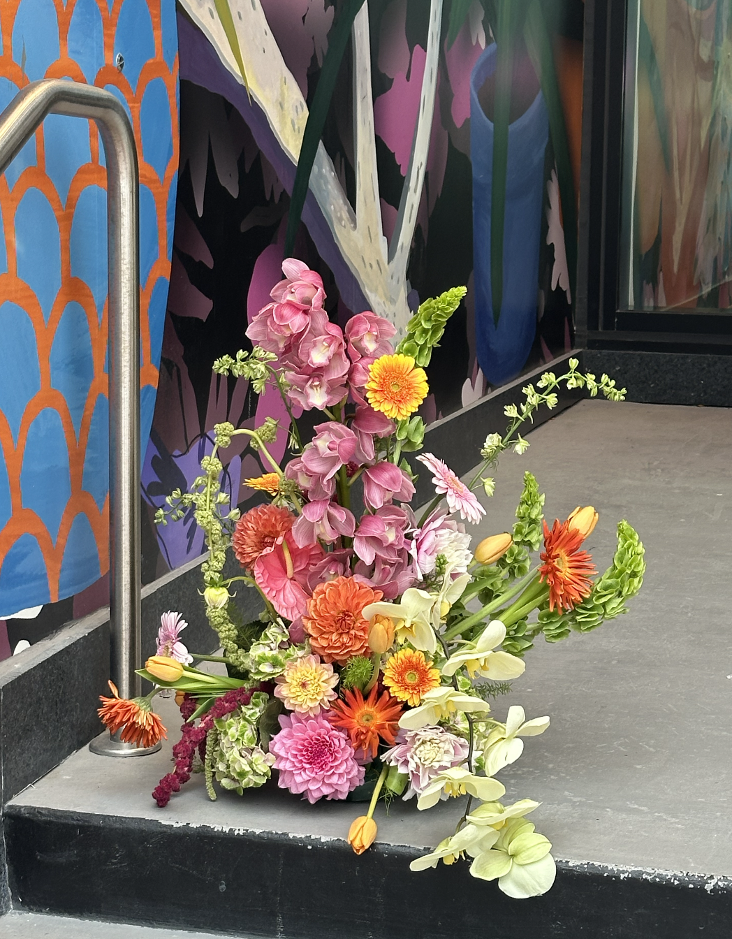A colorful bouquet of flowers placed on the ground in front of a decorative mural.