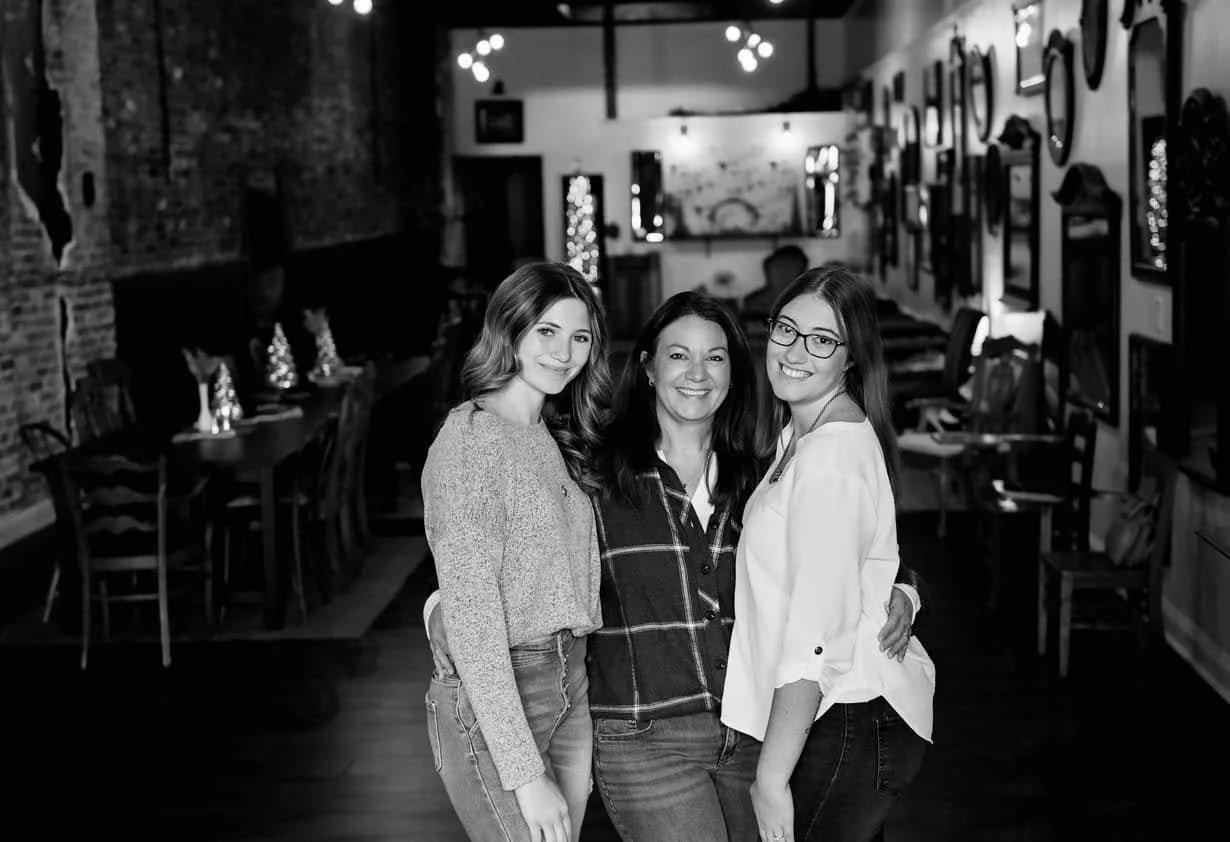Three women standing together in a restaurant, smiling at the camera.