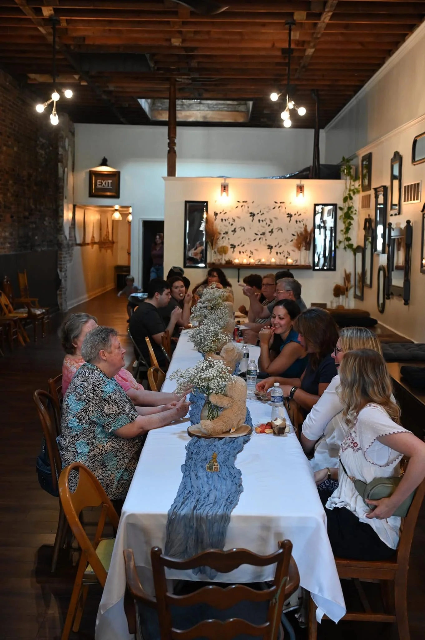 People gathered around a long decorated table at a party or celebration in a cozy, decorated venue.