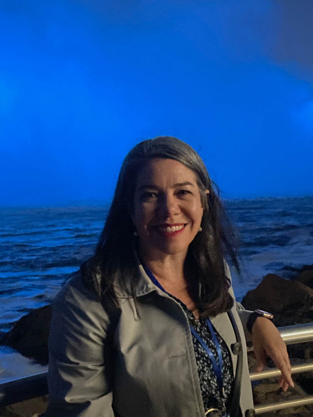 A woman smiling on a boat at sea during evening or night, with a blue sky and some clouds in the background.