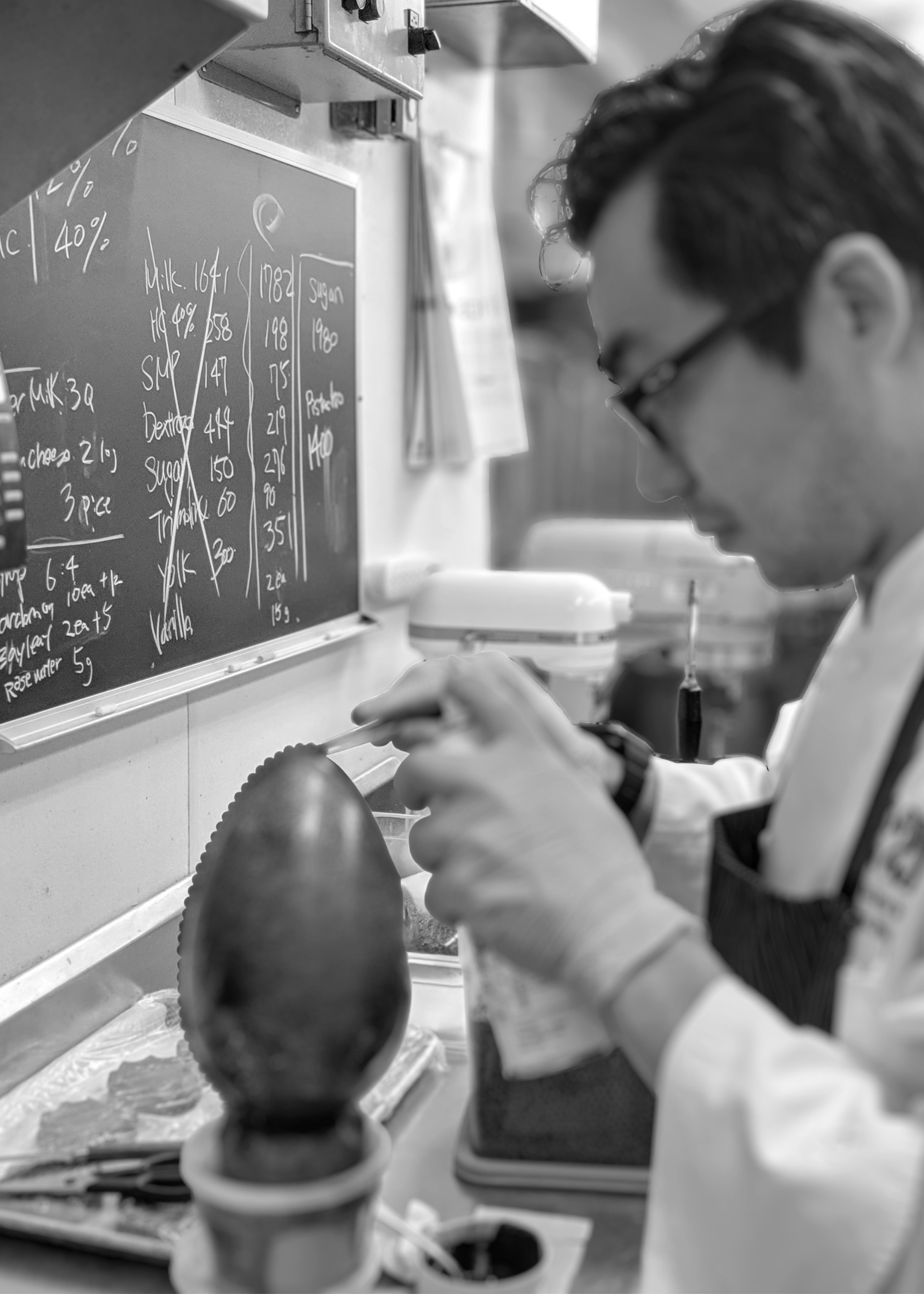 A scientist or researcher in a lab, wearing glasses and gloves, working on a scientific experiment involving a test tube and a mannequin head. The background features a chalkboard with handwritten notes.