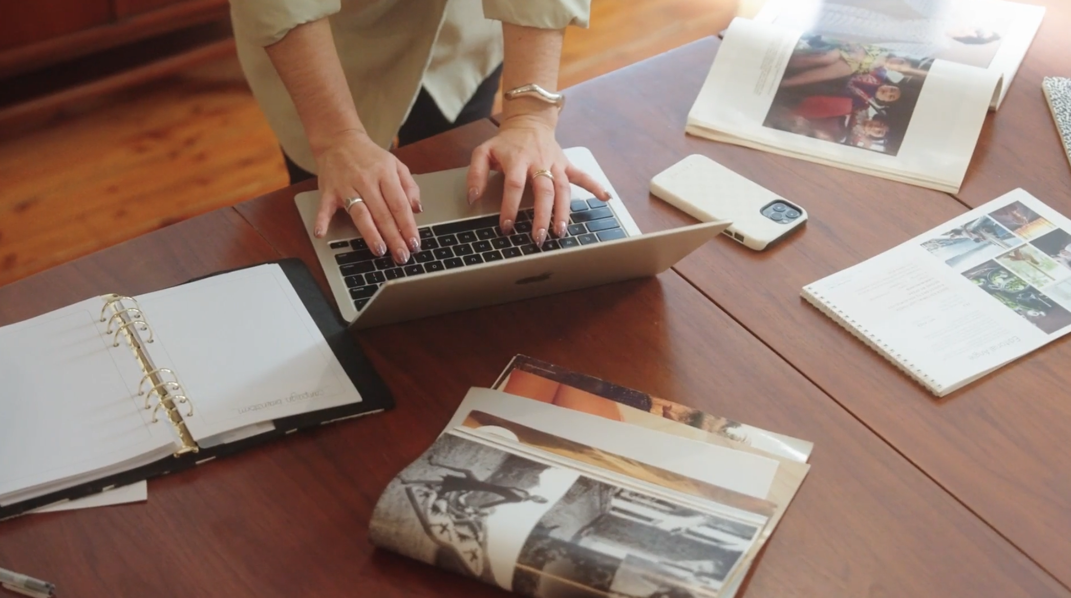Birds eye view of a woman typing away on her laptop with magazines set askew on a desk.