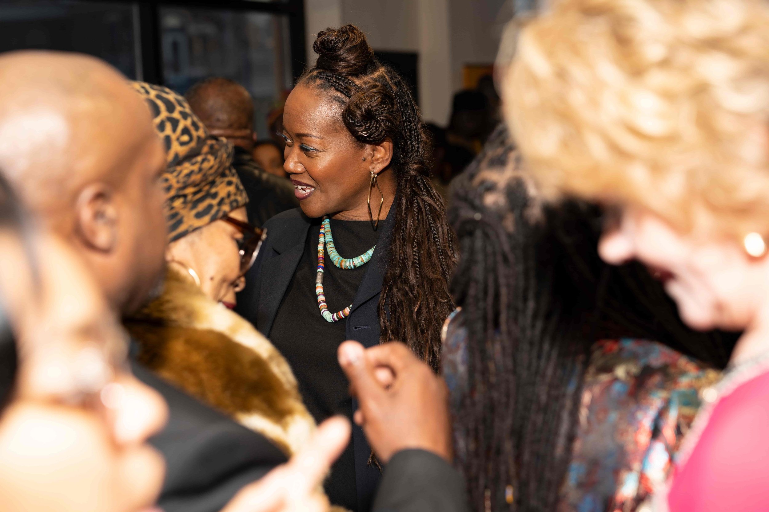 women engaging in conversation at a social gathering, with some wearing patterned clothing and accessories.