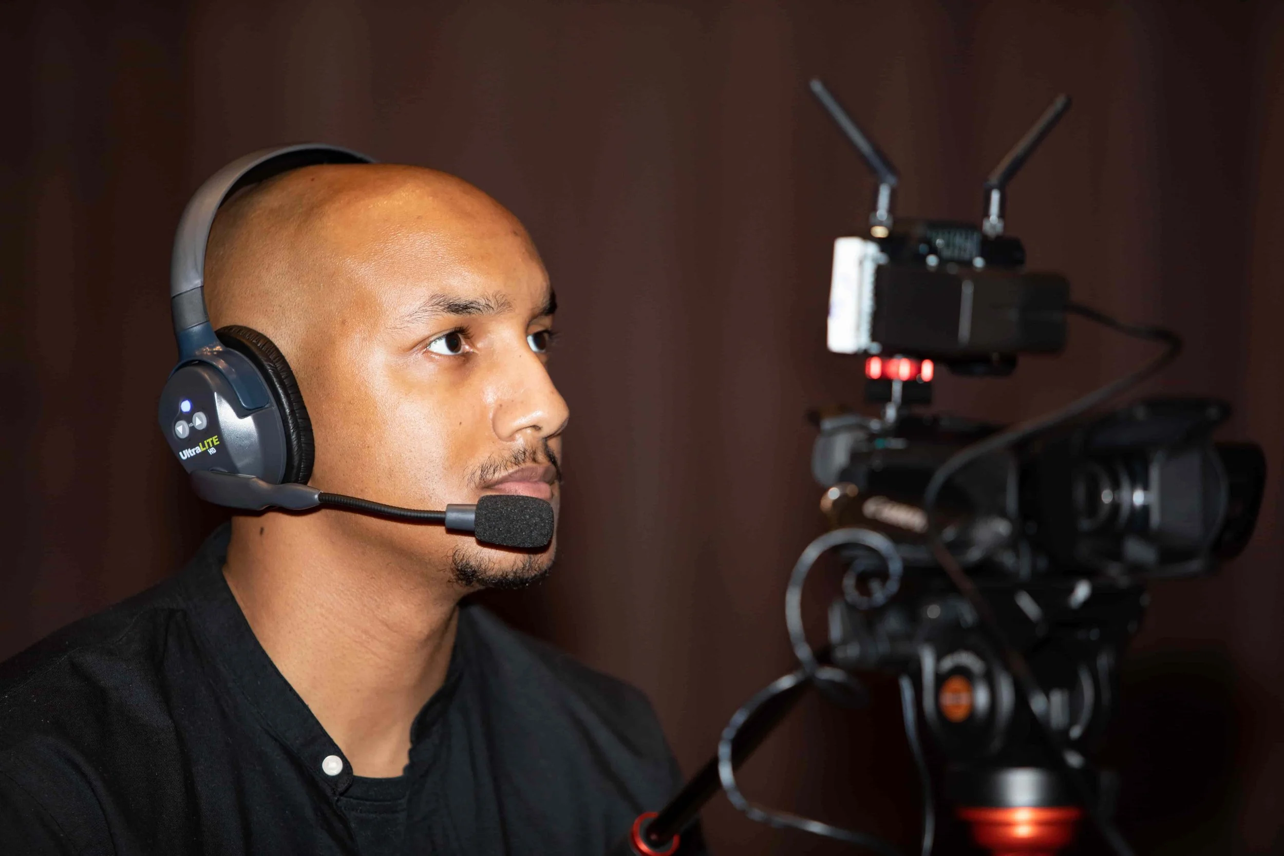Man wearing black shirt and black headphones with a microphone, filming with a professional camera.