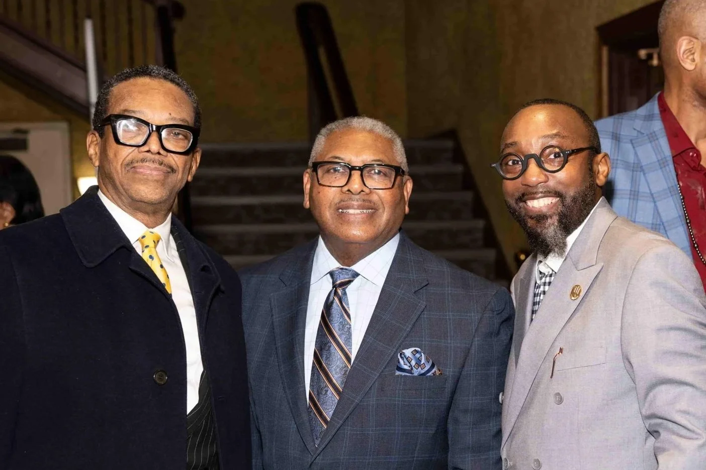 Three men in suits and glasses posing for a photo at an indoor event.