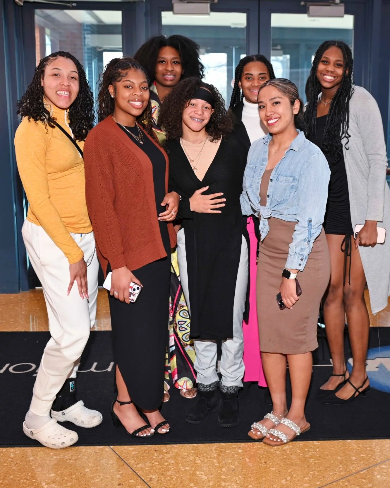 Group of eight women standing together in a lobby, smiling at the camera.