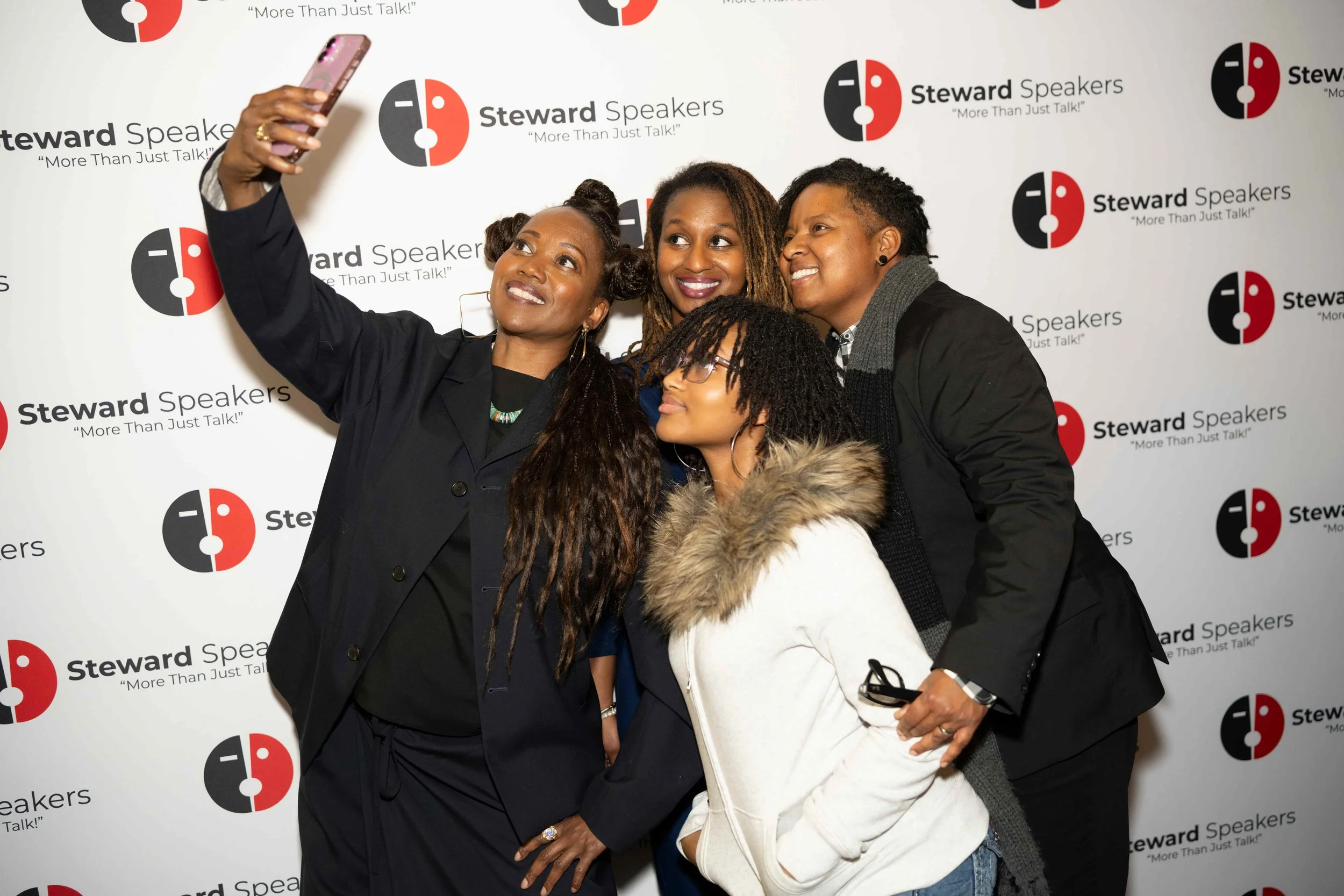 Four women taking a selfie together at a Steward Speakers event, standing in front of a branded backdrop.