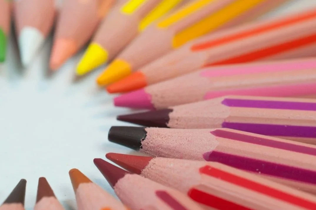 Colorful array of colored pencils arranged in a semi-circle with sharpened tips pointing inward on a white background.