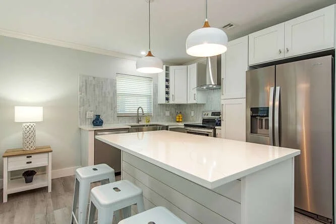 Modern kitchen with white cabinets, a large island, stainless steel refrigerator, oven, and pendant lights over the island.