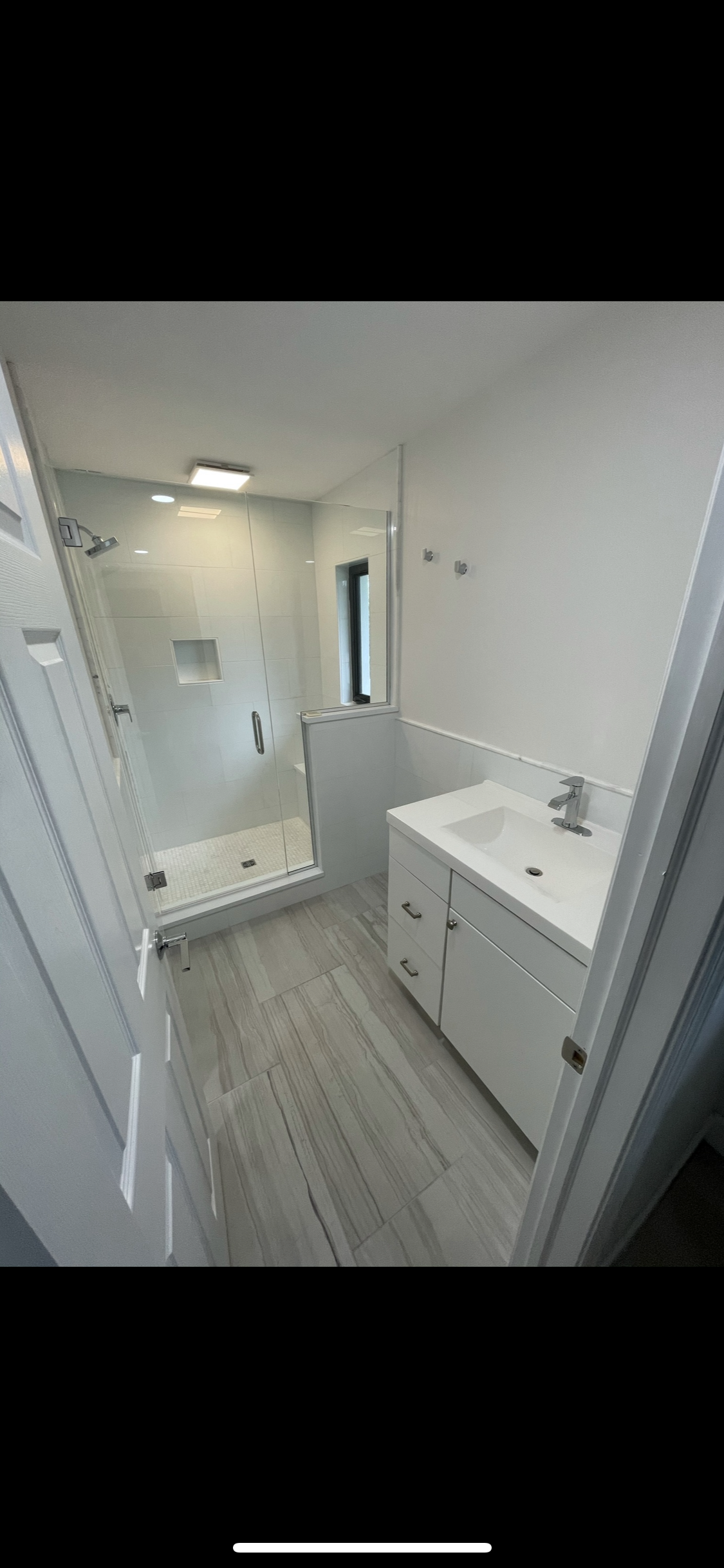 Modern bathroom with a glass-enclosed shower, white vanity with sink, and gray tile flooring.