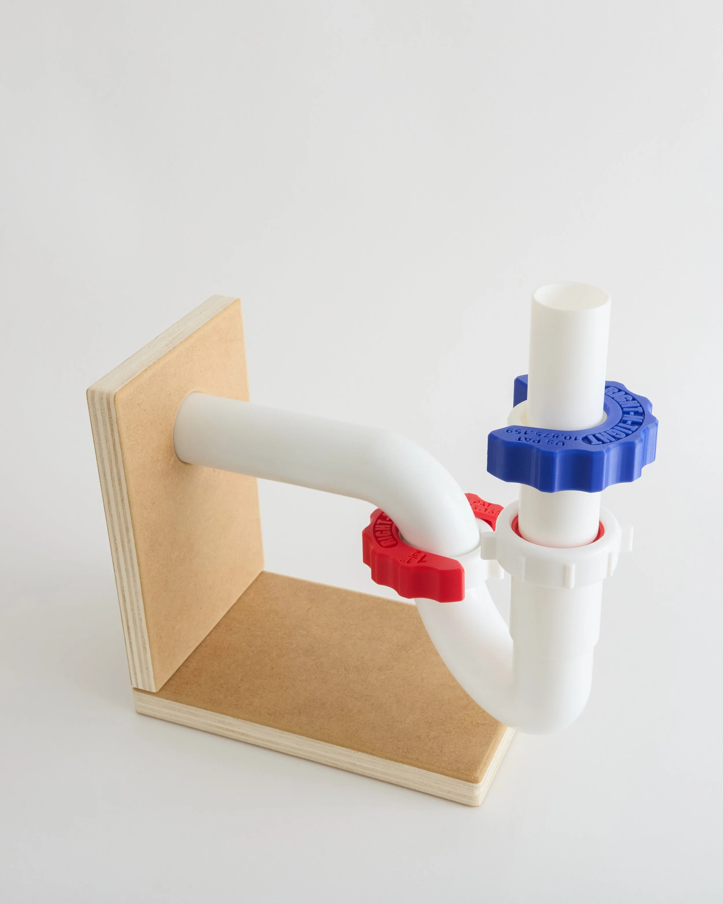 PVC pipe plumbing fitting with red and blue valve handles mounted on a wooden board.