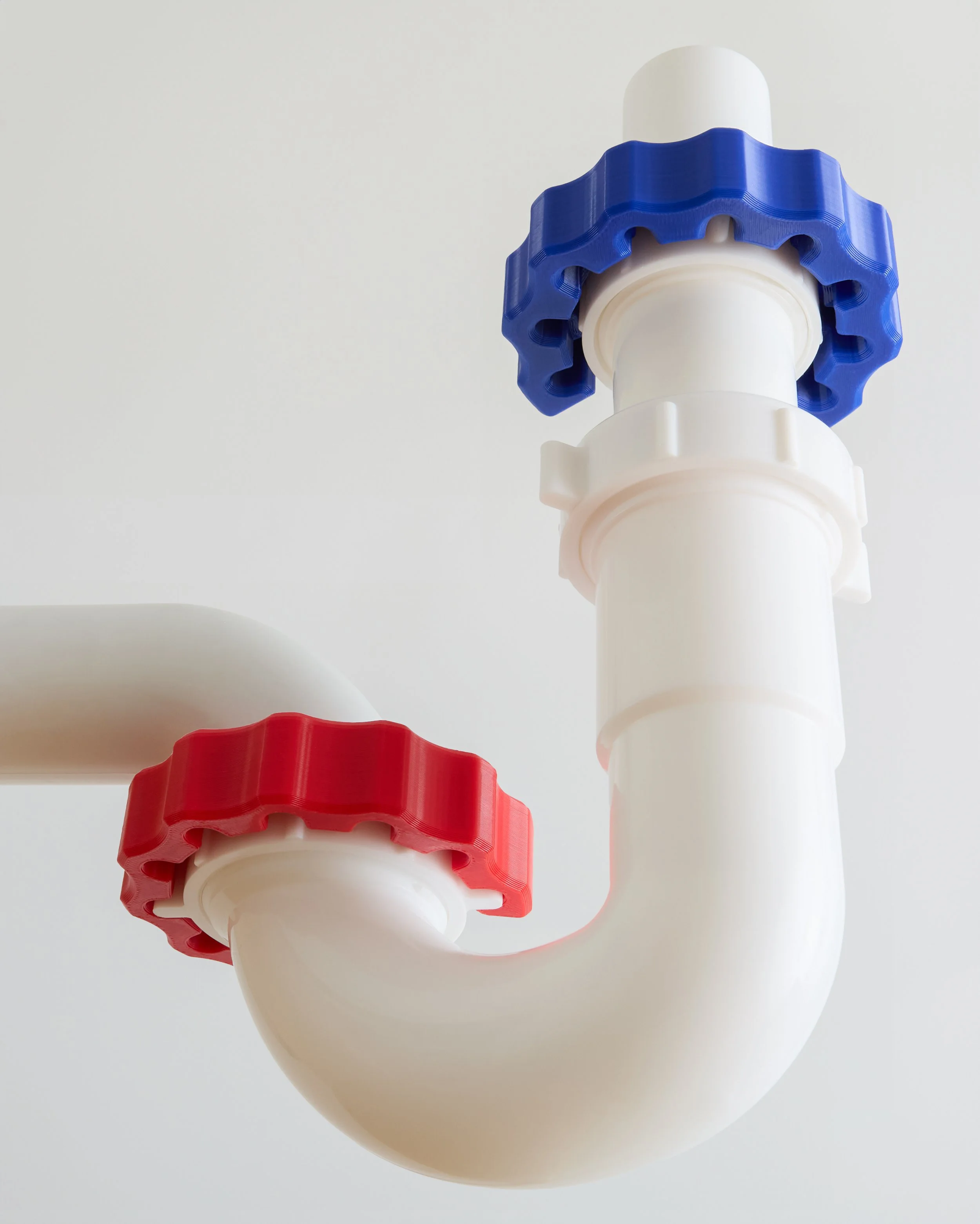 Close-up of a white plumbing pipe with red and blue valves against a white wall.